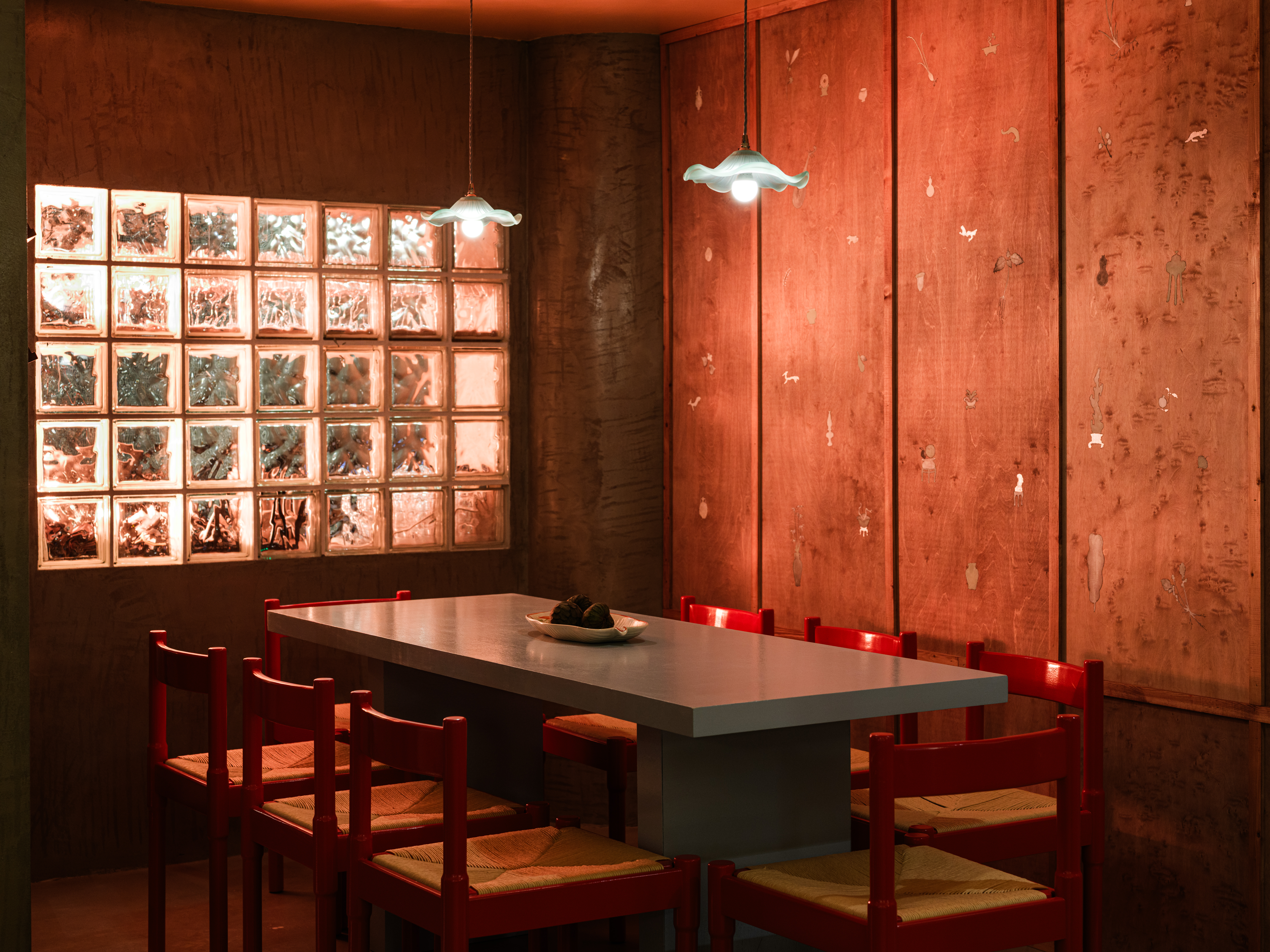 A dramatically lit and designed restaurant pairing cement walls with hand-painted wooden panels, murals, terracotta tiles, chrome accents, and glass blocks.