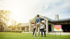 A family of four standing in the front yard of a home next to a "house for sale / sold" sign