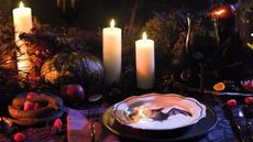 Halloween table with bat plate, purple napkins, black tablecloth and white taper candles