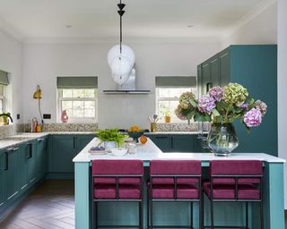 A teal shaker-style kitchen with kitchen island and berry bar stools