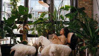 A woman relaxes in a room full of houseplants