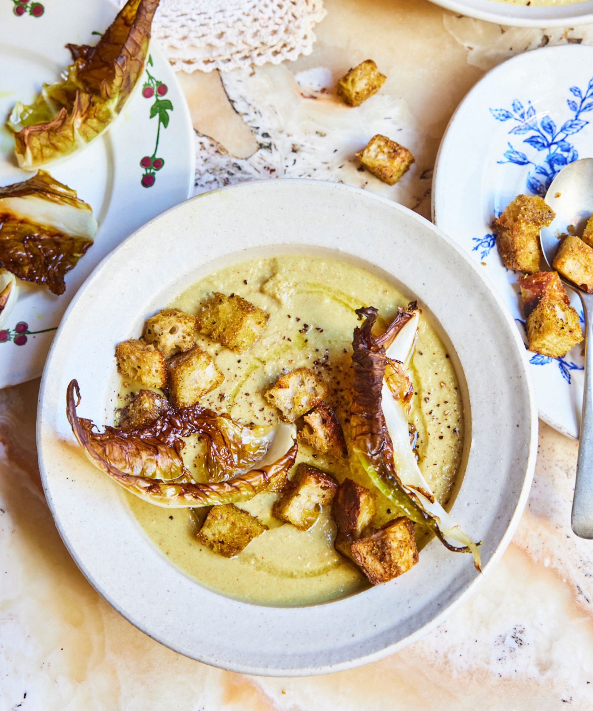 Bowl of cauliflower soup with leaves and croutons on a marble surface with scattered croutons on a blue and white plate