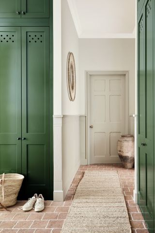 hallway/entryway with green storage doors, brick flooring, stone walls, rug, basket