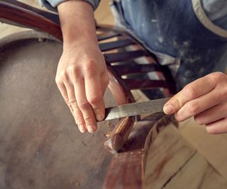 A man sanding the top edge of a wooden antique chair