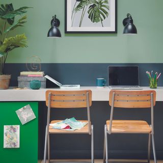 Home office with green walls, two chairs and a long desk.