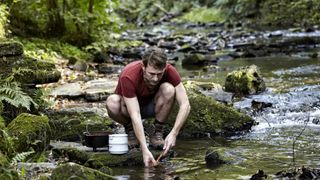 how to clean camping cookware: man cleaning pots in stream
