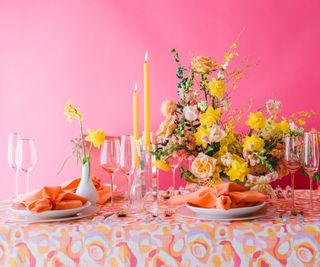 Vibrant tablescape with yellow and peach flowers, yellow candles on a pink background