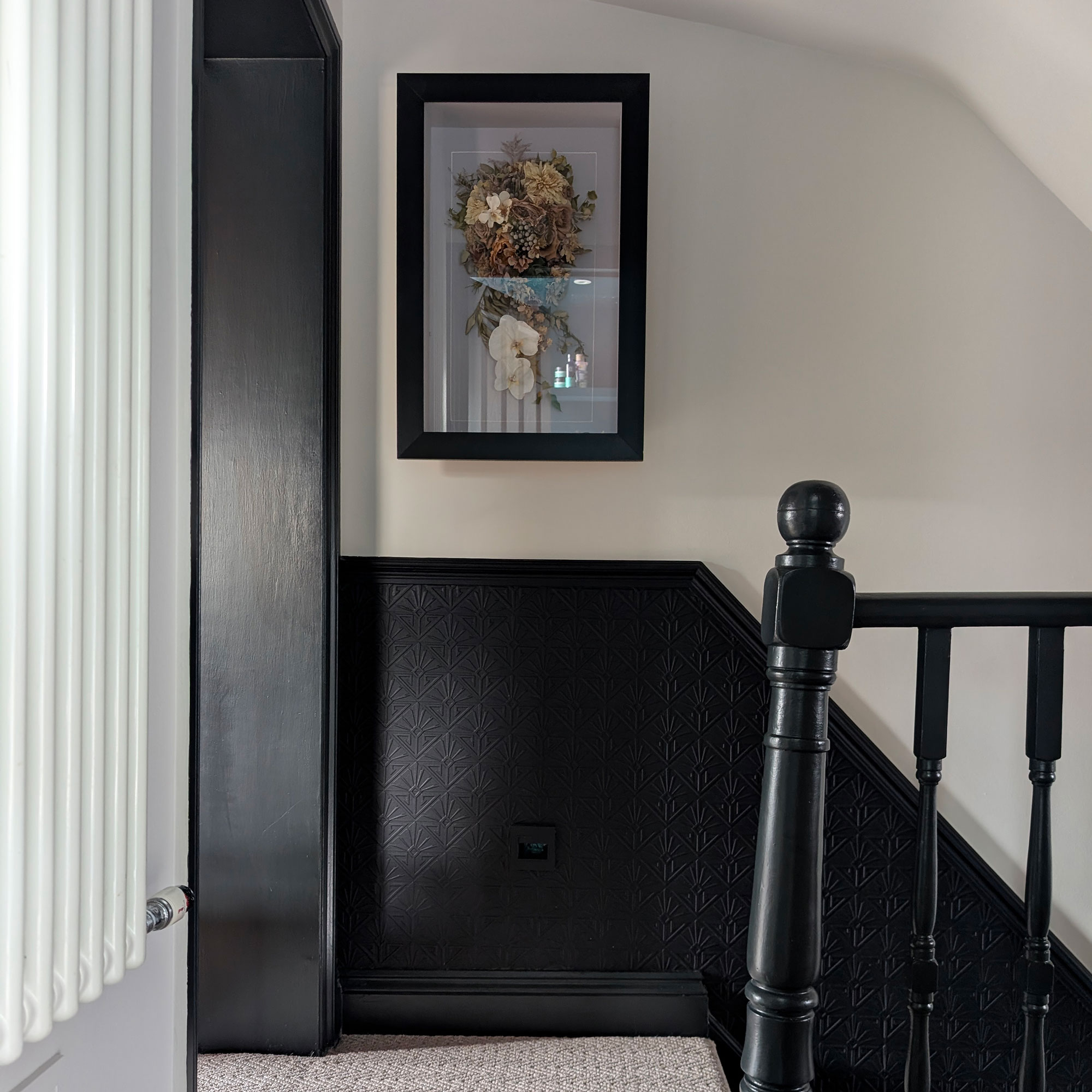 Landing area with banisters and bottom half of wall painted in blue-black, with top half painted white. Framed dried flowers on wall