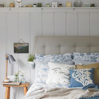 coastal bedroom ideas with grey bed, blue pattered bedding, nautical cushions, weathered stool, shelf with nautical accessories, vintage painting