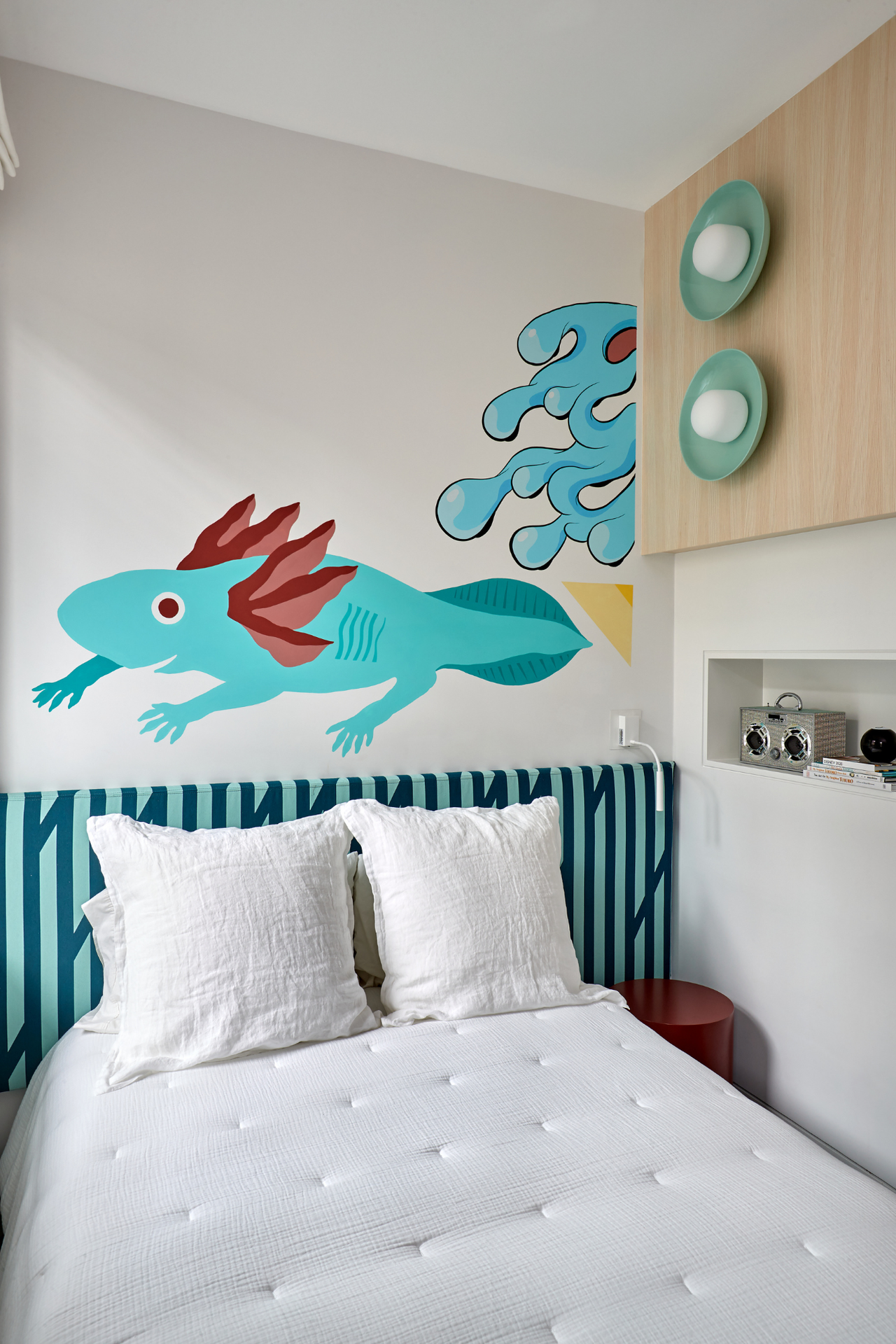 a children's bedroom with a double bed with white bedding and white walls with a lizard artwork on the wall above the bed and a striped blue headboard