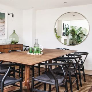 Dining Room decorated in white with a wooden floor, wood dining table with vintage chairs and round mirror. Green accessories and plants. West London home to Gabby Palumbo and her husband Matthew