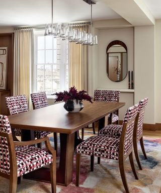 A dining room with a wooden table, pink and red patterned chairs and a colorful rug