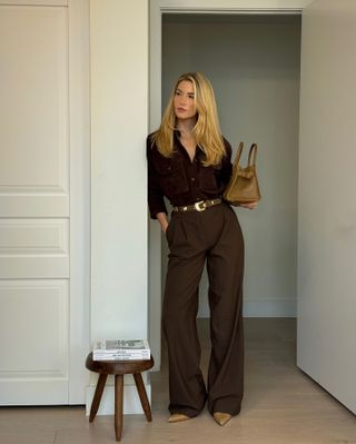 Woman wears a brown button up, trousers, belt and tan pointed toe kitten heels.