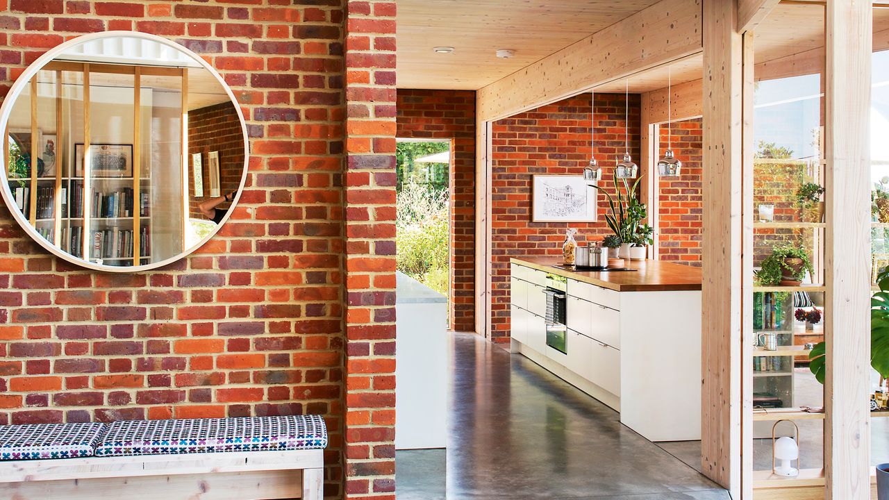 Exposed brick wall, large round mirror and bench, open plan kitchen