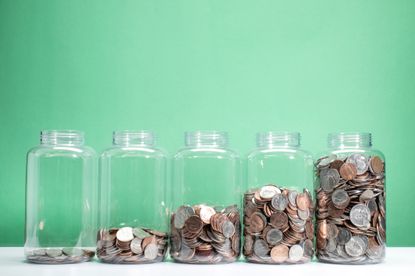5 glass jars containing various US coins in ascending order of fullness, green background