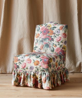 Floral printed chair with skirt in front of linen fabric backdrop on wooden floor