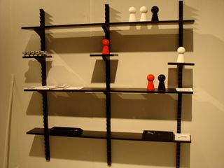 Black 4 level wall shelf with ornaments placed on different levels of the shelf photgraphed on a cream coloured wall