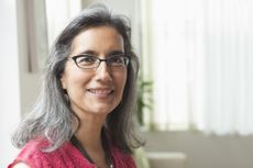 An attractive older woman smiles at the camera. She is wearing glasses and has graying, long hair.