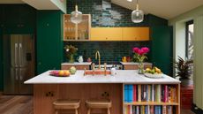 Bright and colorful kitchen with green tiles and yellow kitchen cabinets, as well as green and oak. A kitchen island is placed in the middle with a marble countertop. 