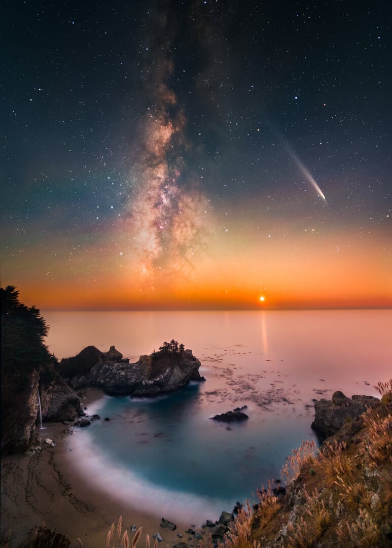 A photo of a pristine rocky beach with the Milky Way, a shooting star, and a setting planet visible in the sky