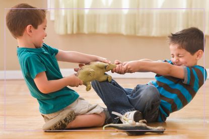 Two young boys fighting over a toy dinosaur