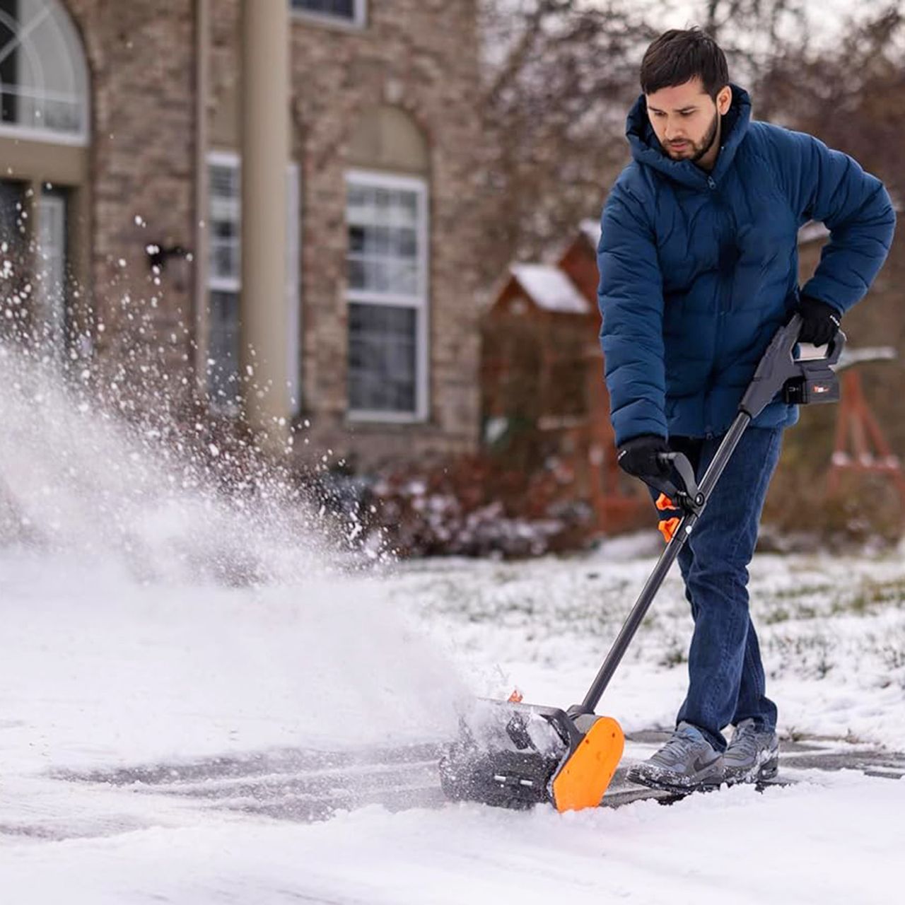Man wearing blue coat and jeans used Wen cordless show shovel in front of house