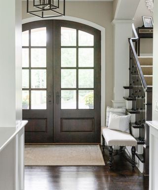 Entryway with arched doors and a modern chandellier, a small bench seat and dark wood floors
