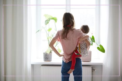 A mum carrying a young girl pictured from behind while staring out the window