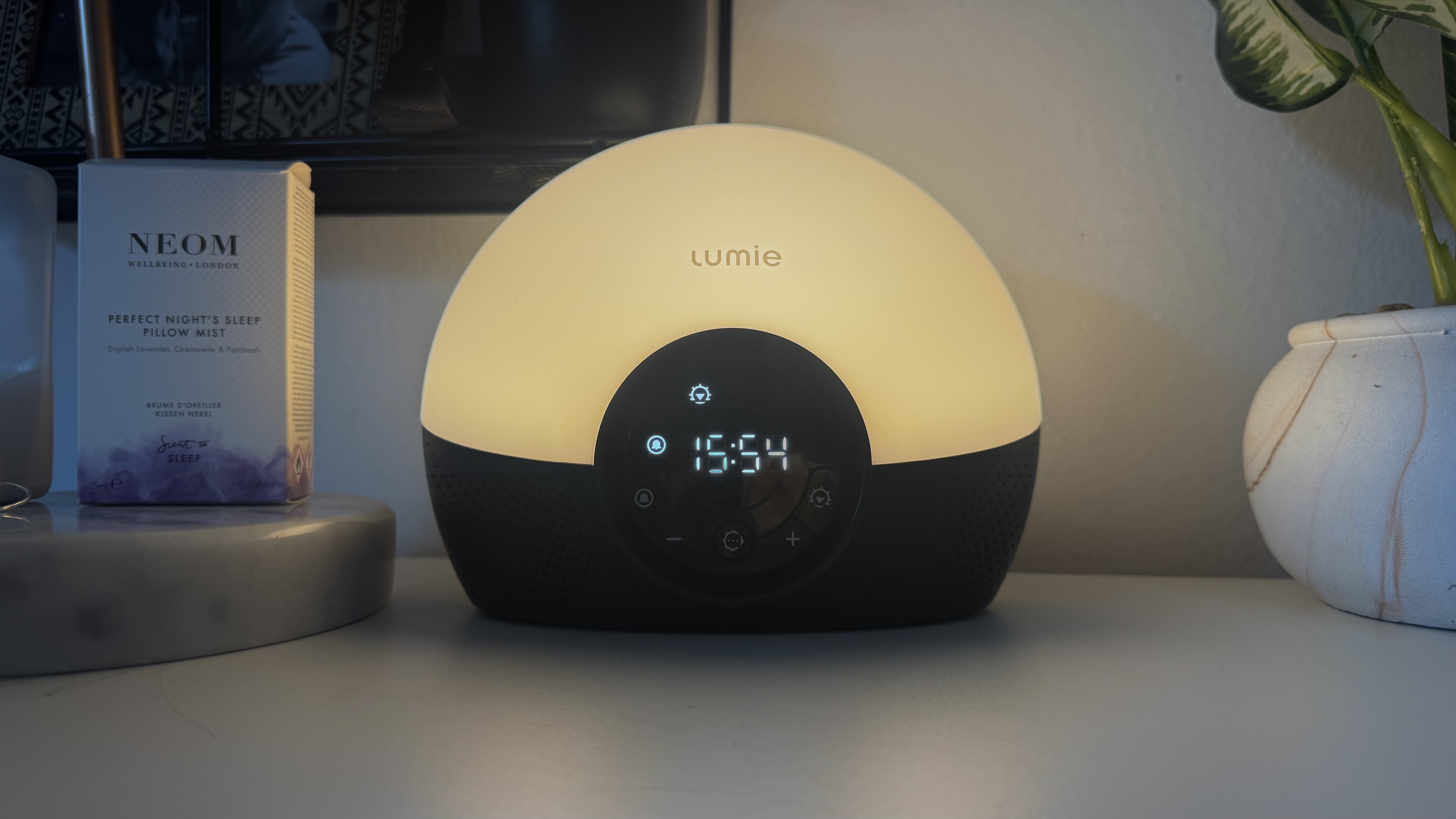 Lumie Bodyclock Glow 150 sunrise alarm clock on bedside table with NEOM pillow spray and plant