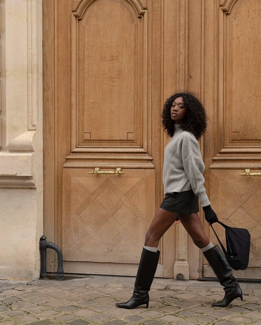 Woman in sweater, skirt, and knee-high boots.