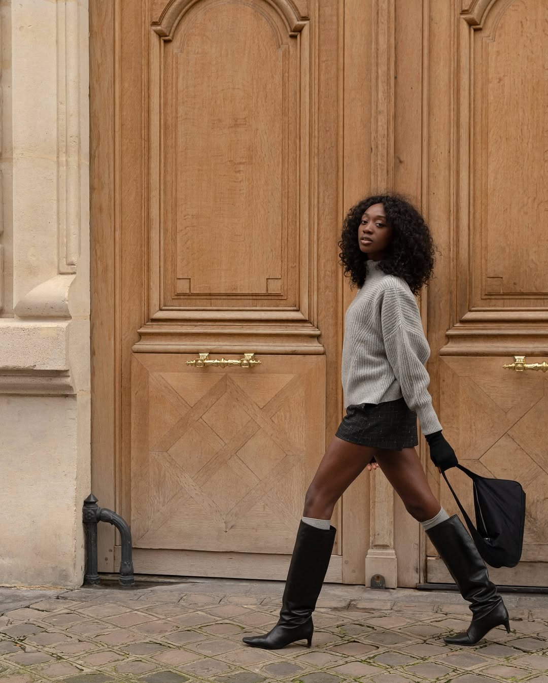 Woman in sweater, skirt, and knee-high boots.