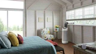 The Frigidaire FGPC1044U1 portable air conditioner sat in a bedroom decorate with a floral chair and blue bed