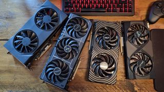 Four budget graphics cards from various manufacturers on a wooden desk, with an RGB-lit gaming keyboard and a gamepad visible above