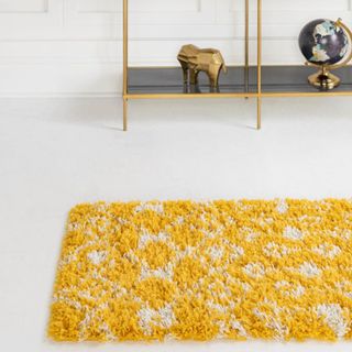 A yellow and white fluffy runner rug sits on top of a white concrete floor