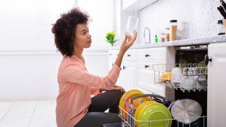 A woman checking a glass while unloading a dishwasher