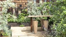 A wooden table and chairs surrounded by raised beds with green shrubs at the RHS Chelsea Flower Show 2026