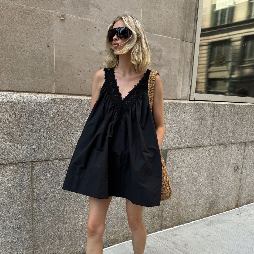 @hoskelsa walks outside wearing a black cotton minidress with leopard print ballet flats and oversized sunglasses.