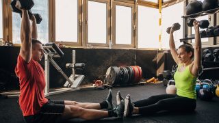 Man and woman perform z press shoulder exercise with dumbbells