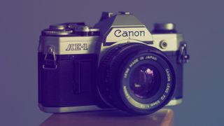 Canon AE-1 film camera on a wooden surface in front of a purple background