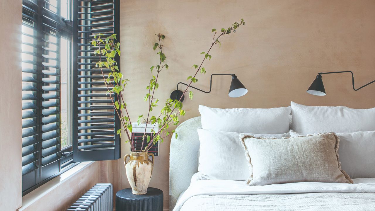 A bedroom painted in a beige shade with a limewash effect, a white bed and black windows