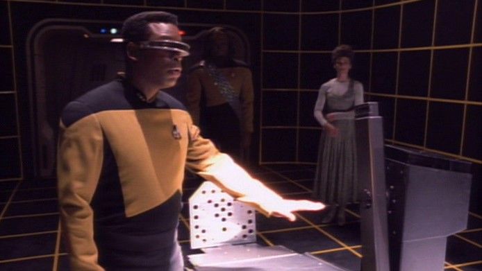 Laforge from Star Trek The Next Generation on the holodeck with hand hovering over a desk. 