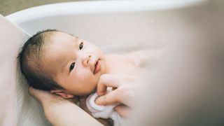 Newborn baby smiles at their mother who is washing them in the bathtub