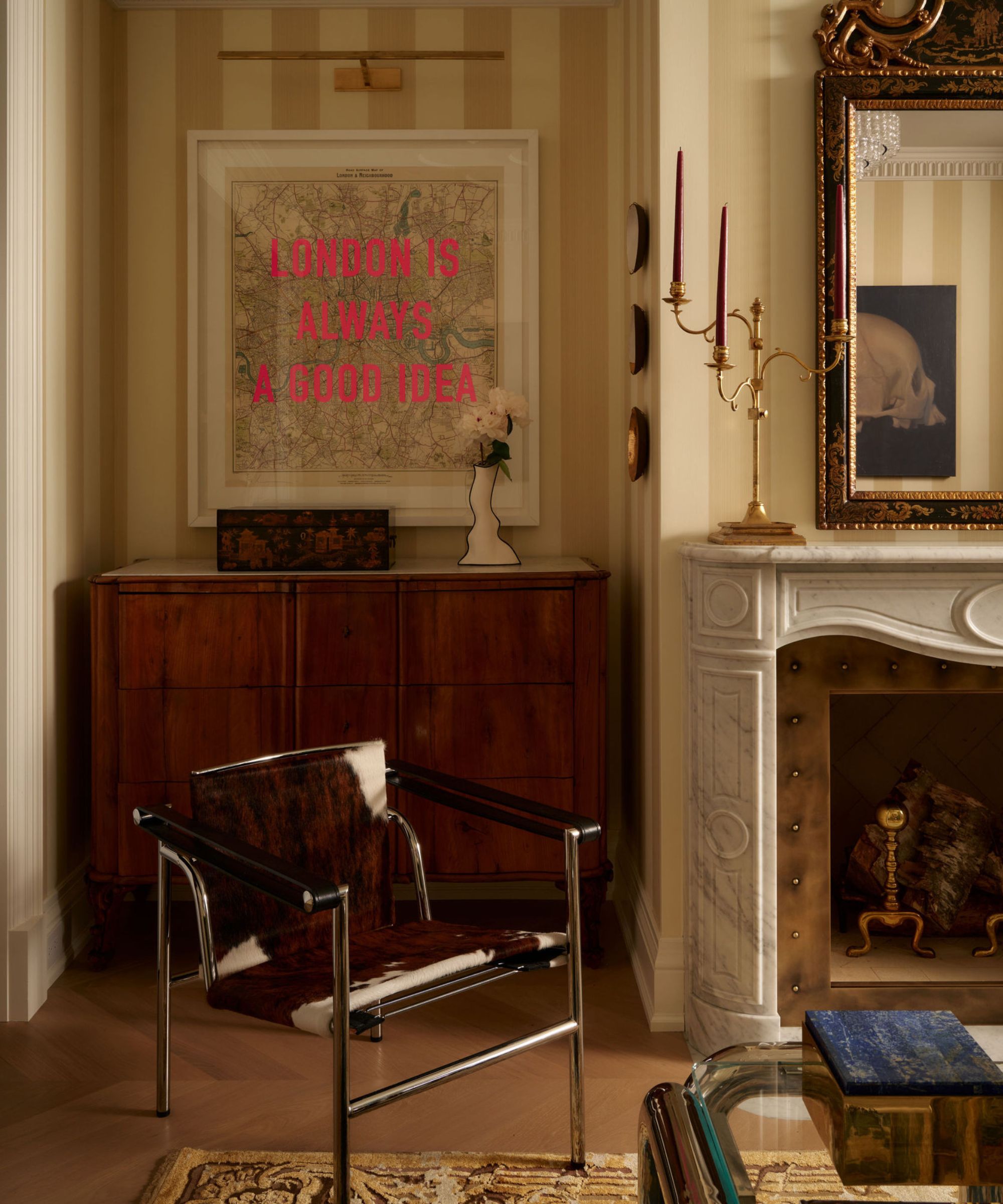 a large living room with yellow striped wallpaper, ceiling molding, vintage rug, marble fireplace, and a cow print chair