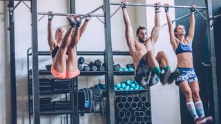 Three people performing toes-to-bar exercise in the gym