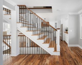 Staircase in white and wood contrast with honeyed wood flooring and white walls throughout.