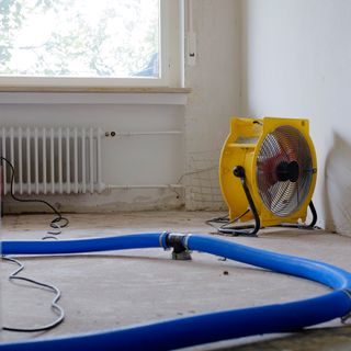Dehumidifier at work in an apartment which is damaged by flooding, with a blue hose pipe