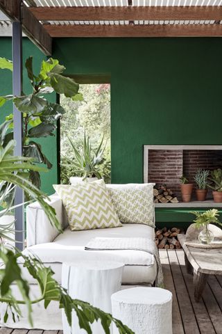 A decked area with dark green wall, outdoor fireplace and beige linen day bed.