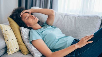 Photo of a woman on a couch with her hand to her forehead like she's sick