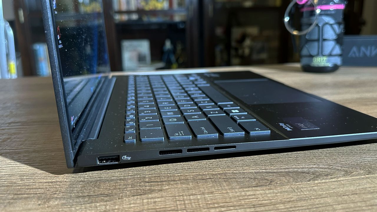 Sideview of Asus Zenbook 14 OLED (Q425M) open on a wooden desk to show thinness and side ports