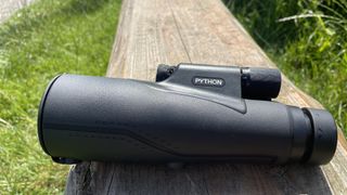 Python 12x52 Range Master Ultra HD Monocular on a wooden log in a park